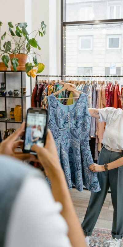A stylish woman holds a dress while a photographer captures the moment in a trendy boutique.
